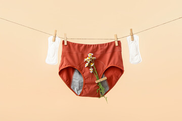 Period panties with chamomile flowers and pads hanging on rope against color background