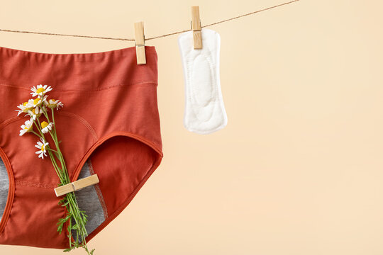 Period panties with chamomile flowers and pad hanging on rope against color background, closeup