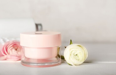 Jar of face cream and ranunculus flowers on wooden table