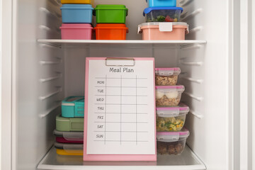 Many different containers with healthy food and clipboard with meal plan in refrigerator