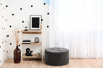 Shelving unit with books, frame, lamps, vase and pouf near color wall