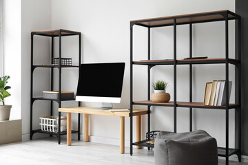 Interior of light room with table, computer screen and shelving units near light wall