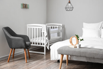 Interior of light bedroom with white crib and armchair