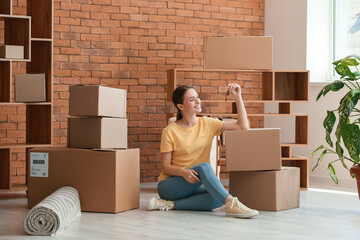 Happy young woman with key sitting on floor in her new apartment