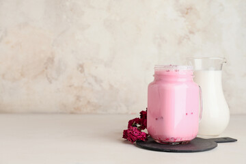 Mason jar of tasty rose latte and jug of milk on light background