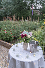 Fototapeta premium Set up next to a sunflower garden, a bouquet of flowers sits on top of a table draped with a white tablecloth, candles, and fairy lights in celebration of a surprise proposal. 