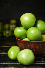 Bowl with green tomatoes on dark wooden table, closeup