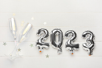 Silver balloons in shape of figure 2023 and glasses for champagne on white wooden background