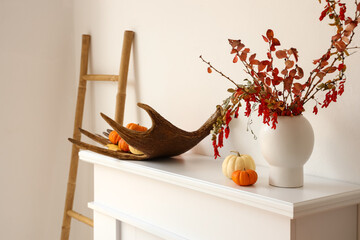 Vase with tree branches, deer horn and pumpkins on mantelpiece near light wall - obrazy, fototapety, plakaty