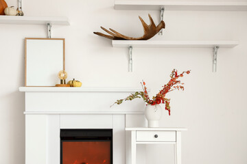 Fireplace with blank frame, table and vase near light wall