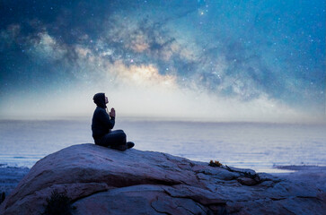 person meditating at night on the mountain under the Milky Way over the ocean