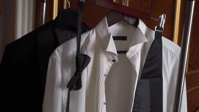 Male suit on a hanger in the bedroom. White shirt, black tuxedo jacket, bow tie. Clothes for the groom for a wedding or for a man for a holiday or event.