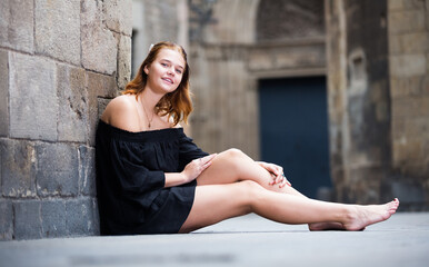 young female sitting barefoot near the stone wall in historical center