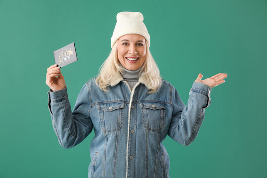 Mature woman in warm clothes and with gift card on color background
