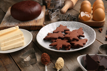 Plate with tasty chocolate Christmas cookies and ingredients on wooden background