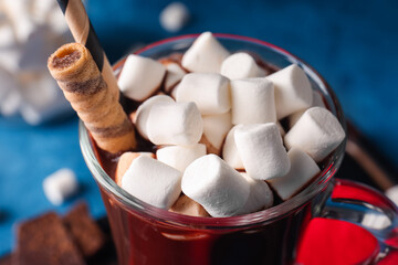 Glass cup of tasty hot chocolate with marshmallows on blue background, closeup