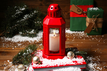 Christmas lantern with burning candle, balls and snow on wooden background