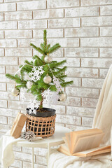 Beautiful Christmas tree in pot decorated with snowflakes and balls on table near beige brick wall