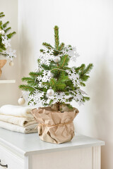 Beautiful Christmas tree in pot decorated with snowflakes and balls on chest of drawers in room