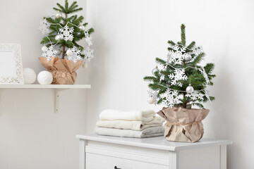 Beautiful Christmas tree in pot decorated with snowflakes and balls on chest of drawers in room