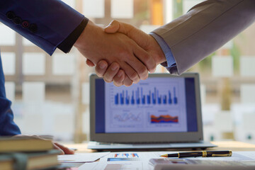 businesspeople shaking hands to end a meeting or negotiation in a sunny office Business handshake and partnership in the office with graph paper and laptop on the table.