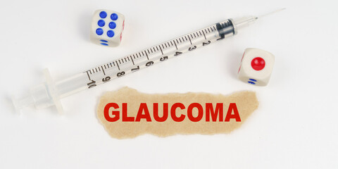 On a white surface lies a syringe, dice and a piece of paper with the inscription -GLAUCOMA
