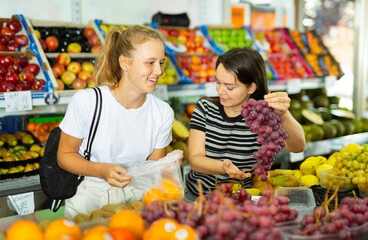 Obraz premium Portrait of teenage girl and her mother who buying fresh red grape at grocery shop
