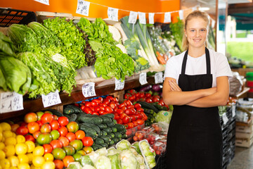 Waist up portrait of pretty young saleswoman posing with fresh fruits and vegetables at grocery store