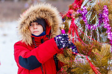 child decorates a Christmas tree in the forest with tinsel