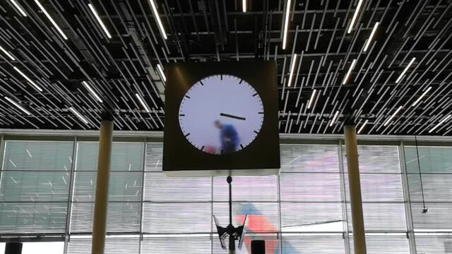 Amsterdam Airport lounge, huge clock being cleaned by man in blue overcoat.