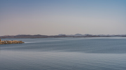 Aswan reservoir in Egypt. Ripples are visible on the calm surface of the blue water. In the distance, against the background of the azure sky, a picturesque mountain range