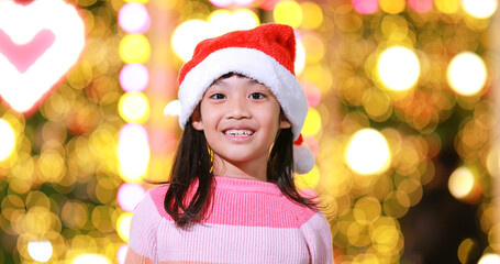 New year anticipation.The cute little girl Wearing a red Christmas hat and beautiful color shirt on a christmas background with bokeh lights .Have fun and have fun during this important season.
