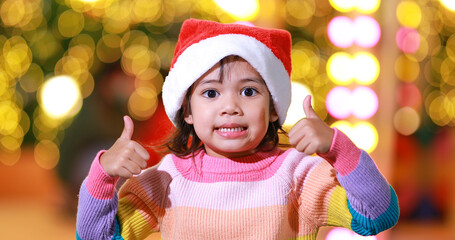 New year anticipation.The cute little girl Wearing a red Christmas hat and beautiful color shirt on a christmas background with bokeh lights .Have fun and have fun during this important season.