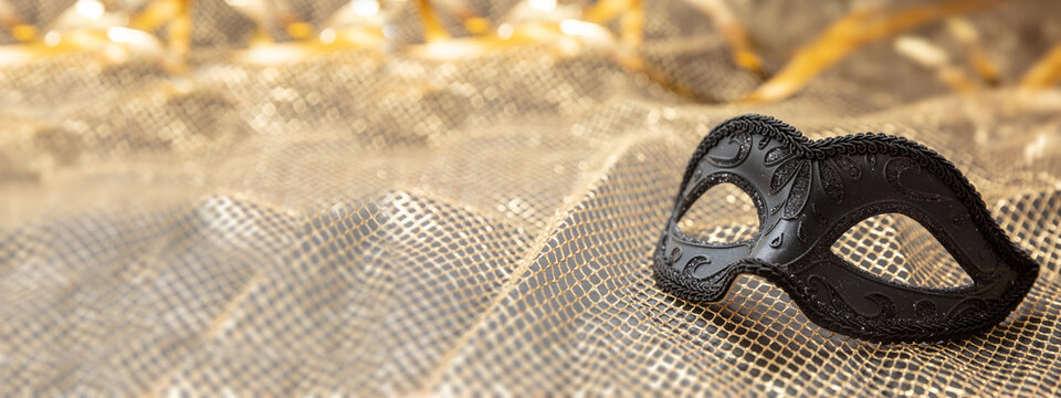 Carnival Venetian black mask on golden shiny festive background, female disguise, masquerade