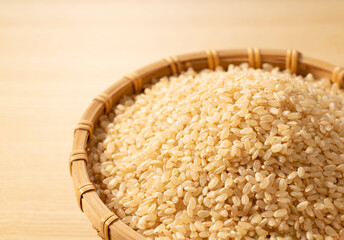 Brown rice in a bamboo colander set against a wooden background.