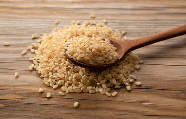 Brown rice in a wooden spoon placed on a wooden background.