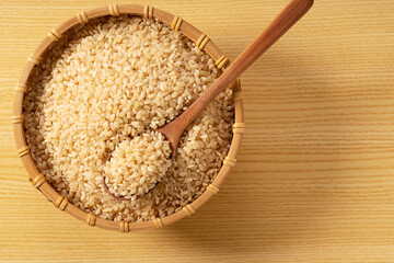 Brown rice in a bamboo colander and a wooden spoon on a wooden background.