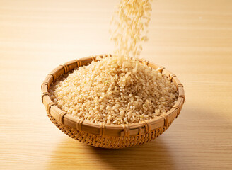 Pouring brown rice into a bamboo colander placed on a wooden background.