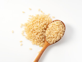 Brown rice in a wooden spoon placed on a white background. - obrazy, fototapety, plakaty