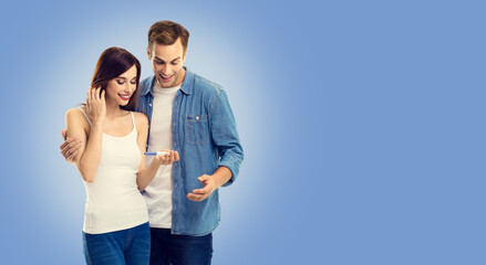 Love, new parents and happy family concept - young happy couple, finding out results of a pregnancy test. Man and woman at studio shot image. Blue color background.