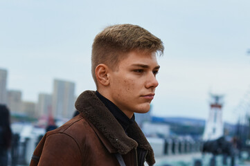 Portrait of a young Caucasian blond guy in a warm leather brown jacket. Skin acne. Undercut...