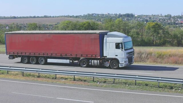 A truck with a red trailer is driving along the highway. The truck is driving along the road. Delivery of goods by truck