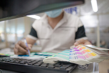 Focus young Asian man wearing medical mask hand holding a color palette sample of different colors for customers to chose from while renovating or redesigning factory interior. Industry concept.
