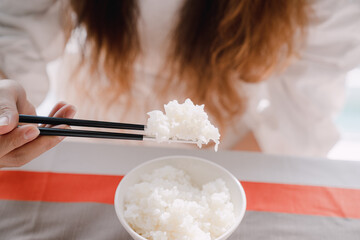 A woman holding white rice with chopsticks.