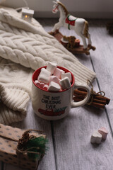A mug with marshmallows, a white sweater, toys on a light photo background.
