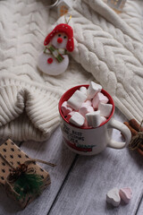 A mug with marshmallows, a white sweater, toys on a light photo background.