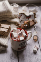 A mug with marshmallows, a white sweater, toys on a light photo background.