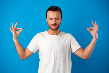 Focused handsome young man meditating on camera iover blue background