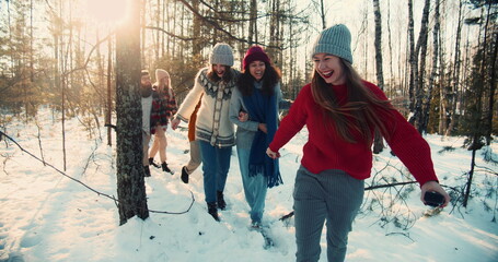 Happy group of smiling multiethnic friends walk along snowy winter forest hike path at holidays weekend slow motion.
