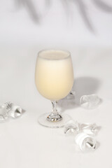 Glass of chilled vanilla milkshake on white table with ice cubes